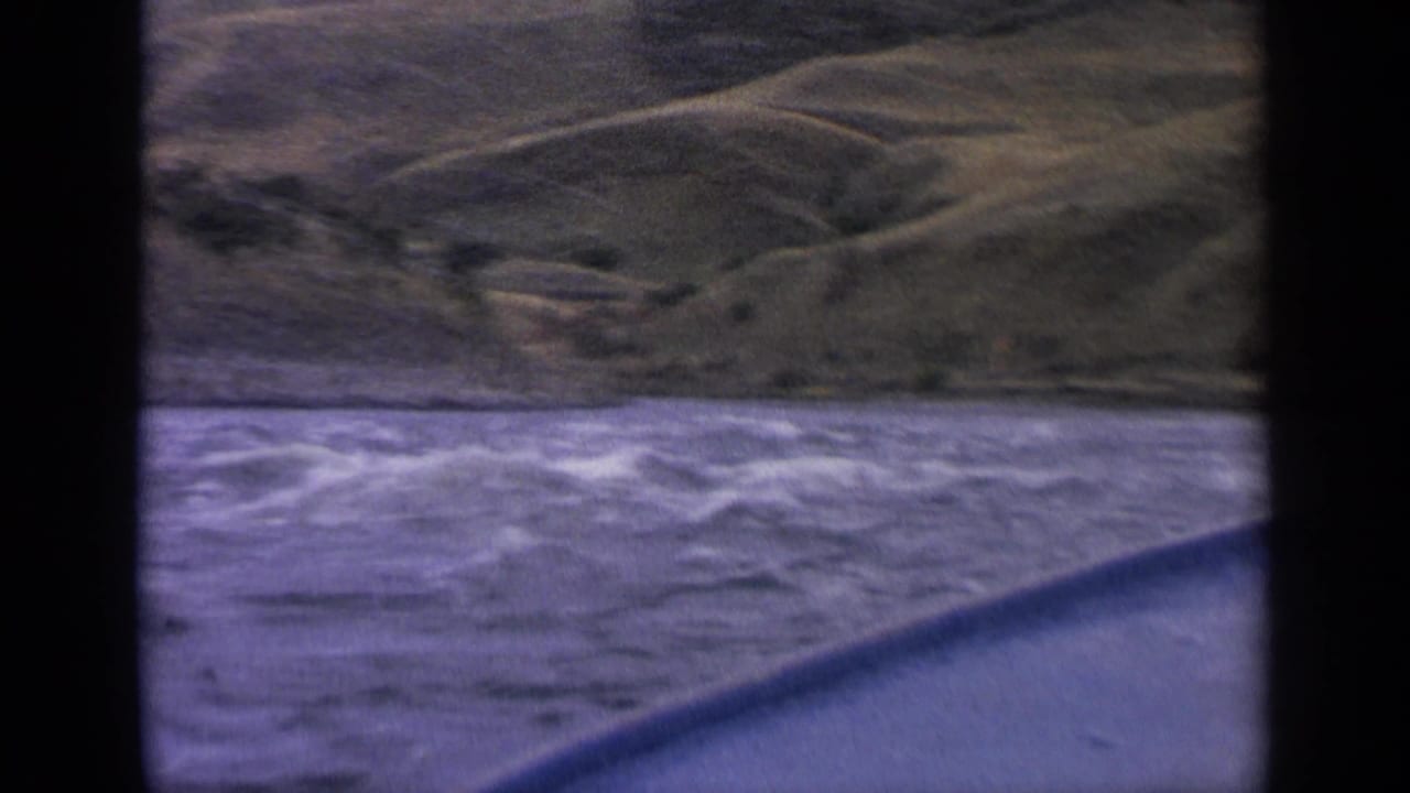 1963 Idaho river view from a boat, with white-capped water, a curved foreground edge, and green hills rising beyond the shoreline.