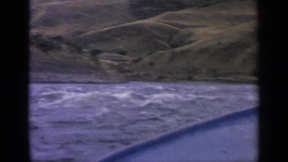 1963 Idaho river view from a boat, with white-capped water, a curved foreground edge, and green hills rising beyond the shoreline.