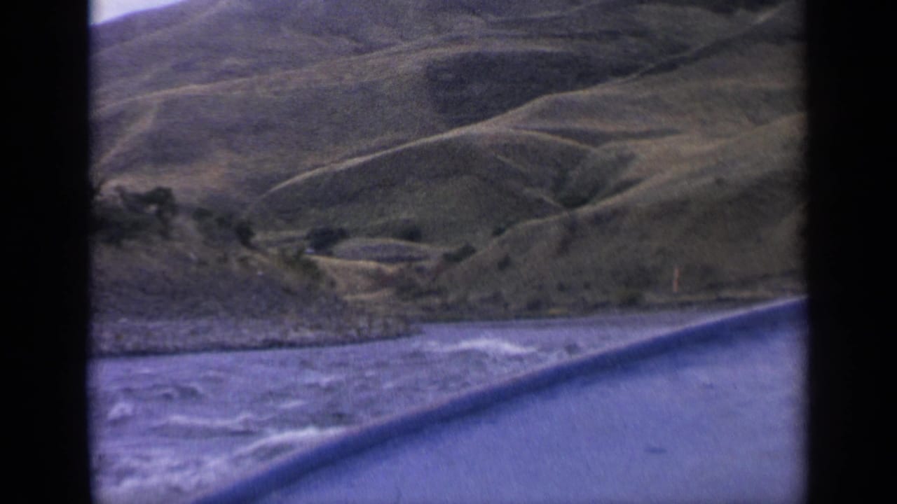 Motorboat view over choppy river water toward rolling hills and a rocky bank.