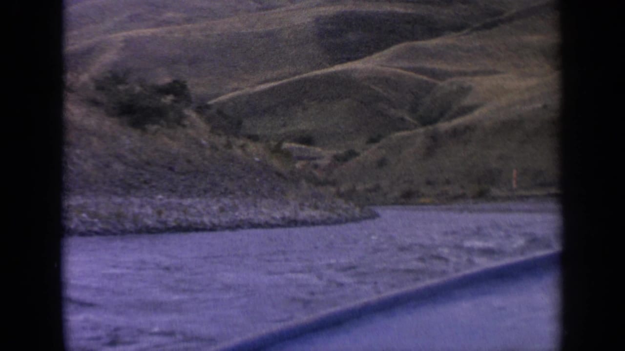 1963 Idaho road-trip view of rippled water, gravel shoreline, and rolling hills through a vehicle window.