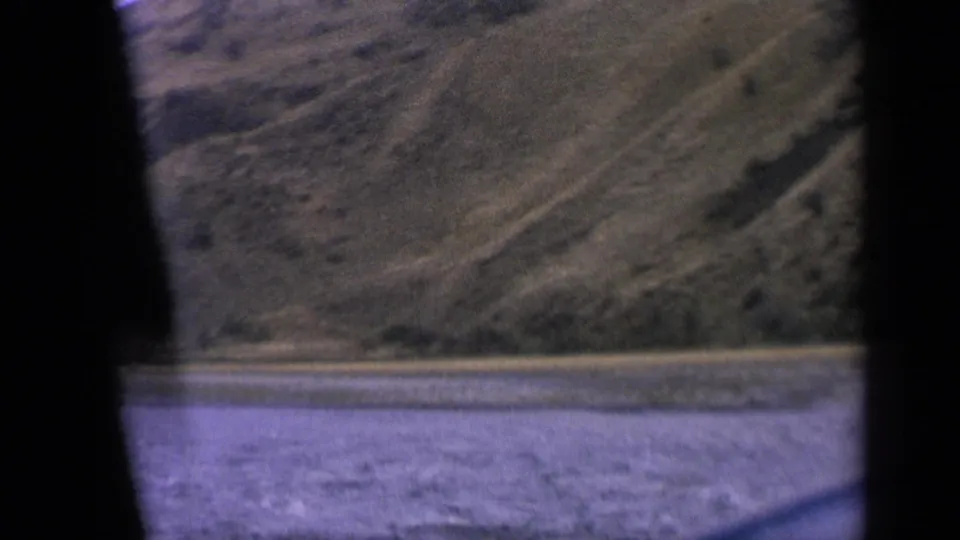1963 Idaho travel view showing water, low shoreline, and scrub-covered hills through a car-window opening.