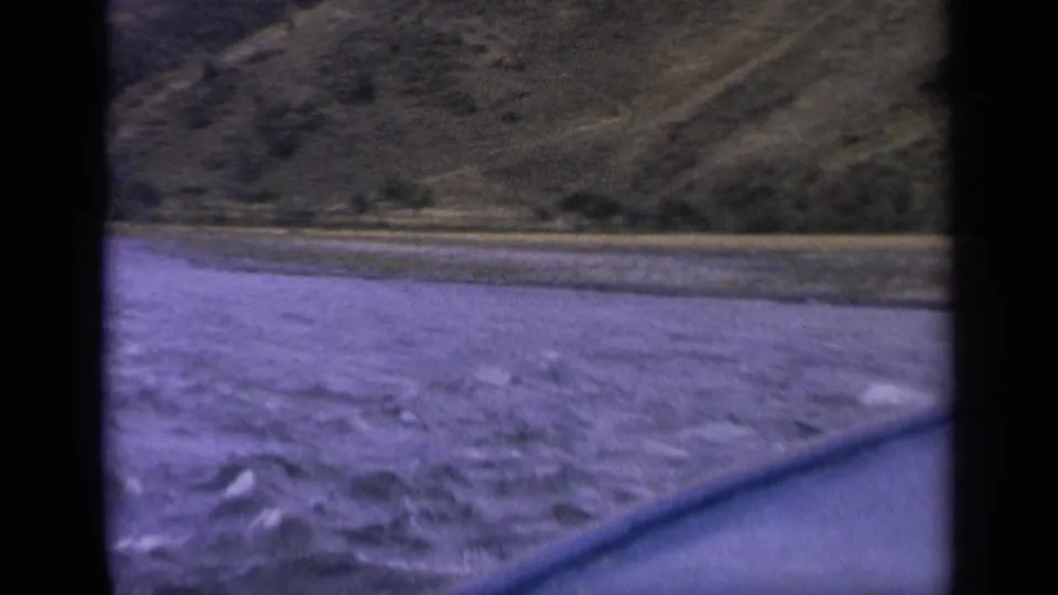 1963 Idaho 8mm frame looking from a small boat across choppy water toward dry rolling hills.