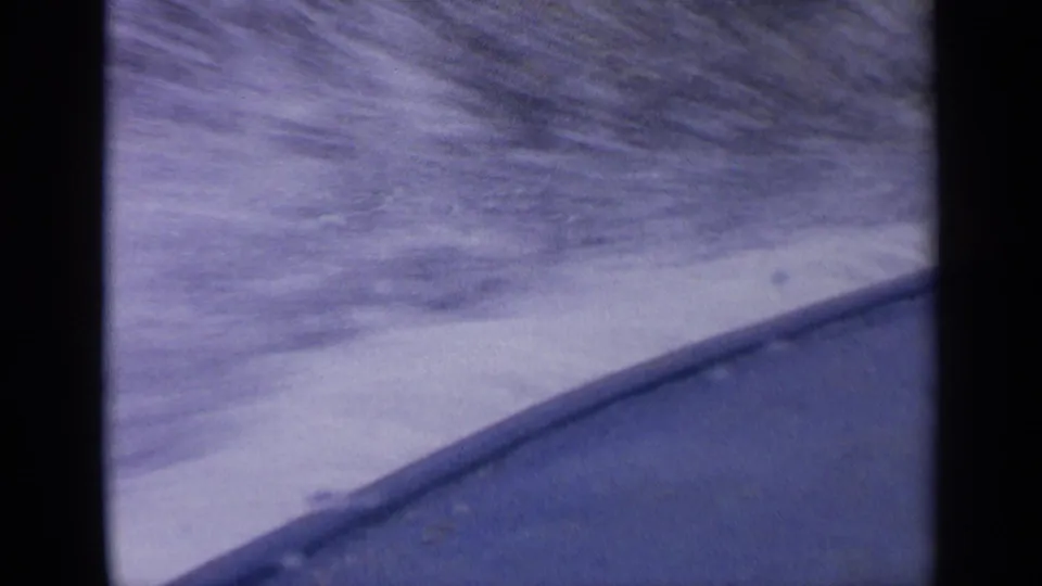 Soft 1963 Idaho 8mm frame with the boat edge at lower right, choppy water, and sloped hills beyond.
