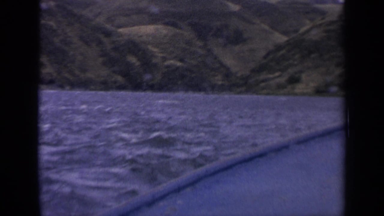 1963 Idaho 8mm frame showing rippled blue lake water, a boat edge, and green hills beyond the shoreline.