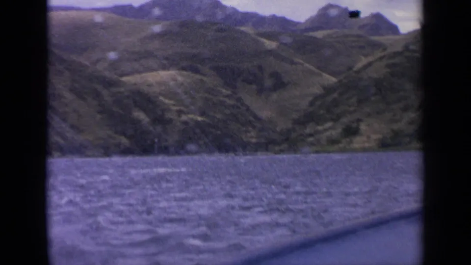 1963 Idaho 8mm frame with rolling mountain terrain above rough lake water, filmed from a swaying boat perspective.
