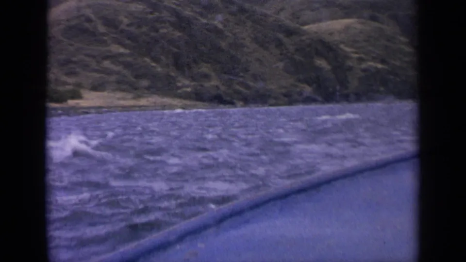 Final 1963 Idaho lake frame showing whitecaps beside the boat edge and rugged shoreline hills in soft 8mm color.