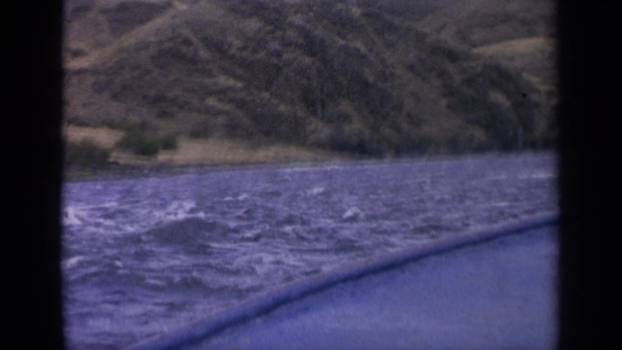 1963 Idaho boat-window view of rough blue river water, whitecaps, and a distant green-brown hillside shoreline.