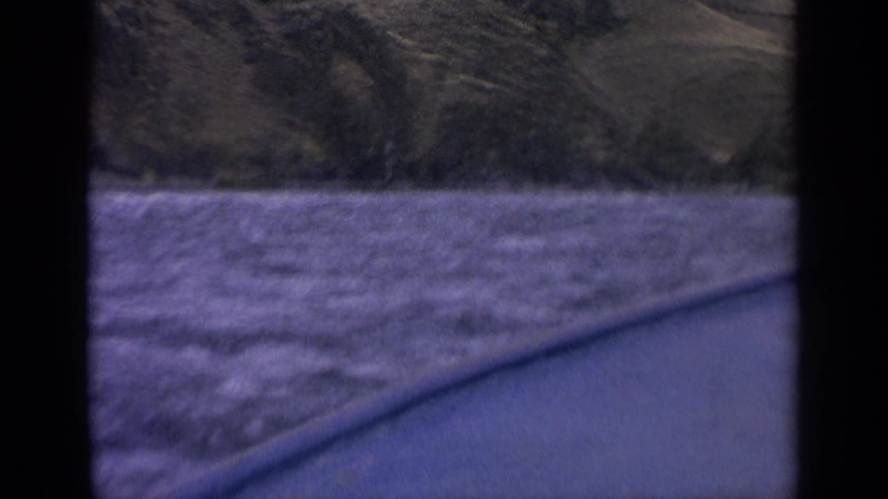 1963 Idaho home-movie frame showing rough river water, a low shoreline, and hillside terrain from inside a boat.