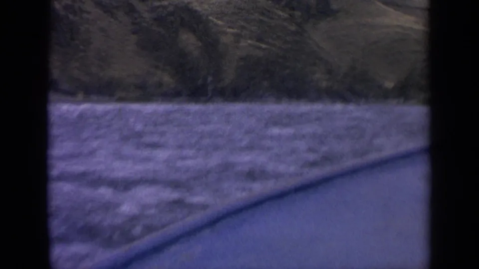 1963 Idaho home-movie frame showing rough river water, a low shoreline, and hillside terrain from inside a boat.