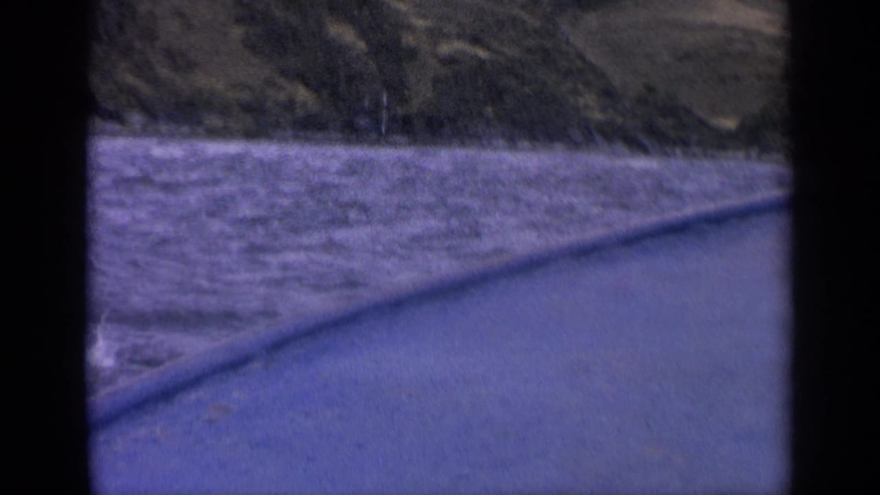 1963 Idaho lake footage showing rippled water, distant hills, and a diagonal boat edge in a soft, purple-tinted 8mm frame.