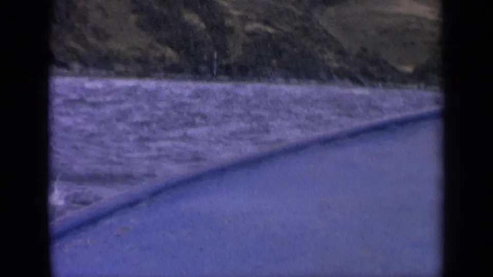 1963 Idaho lake footage showing rippled water, distant hills, and a diagonal boat edge in a soft, purple-tinted 8mm frame.