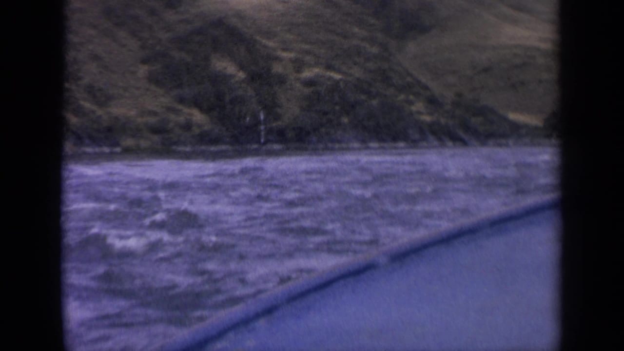Rushing water and hillside seen from the side of a boat.