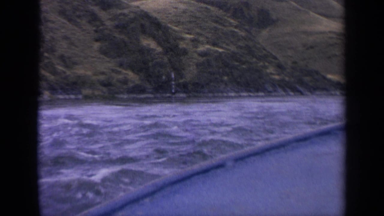 Rough water and grassy shoreline seen past a blue boat edge and dark frame borders.