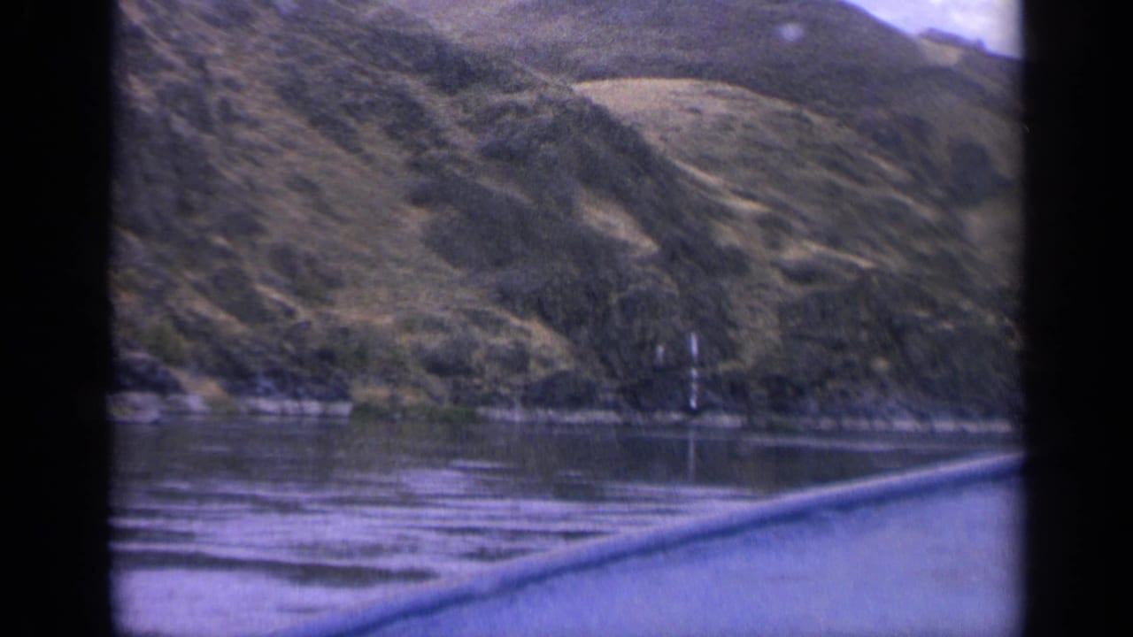 Calm lake with a rugged, tree-dotted mountain shoreline viewed past a dark frame edge.