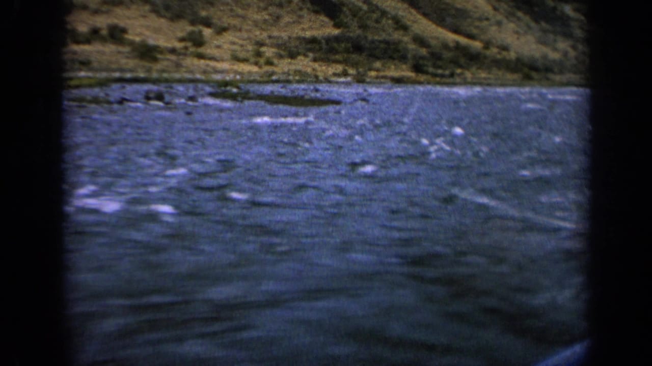 1963 Idaho river scene with textured blue water, white surface streaks, and a dry hillside in the background.