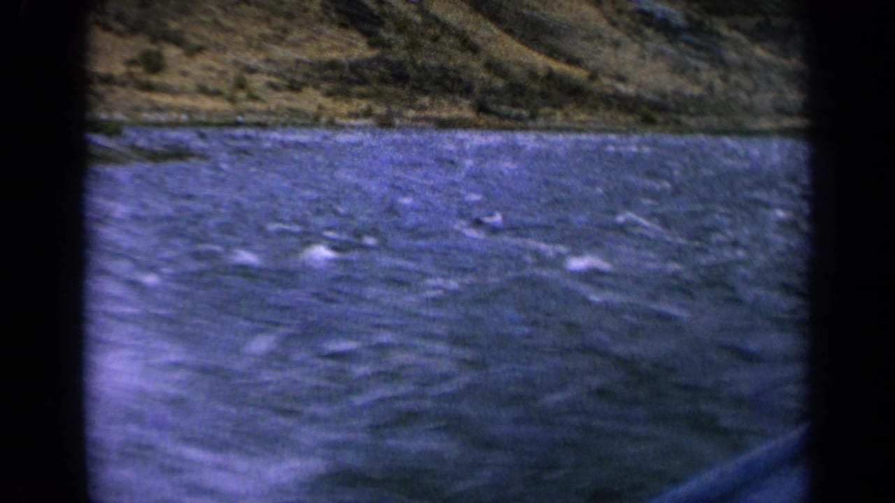 1963 Idaho 8mm frame showing rushing river water with whitecaps and a rugged hillside beyond.