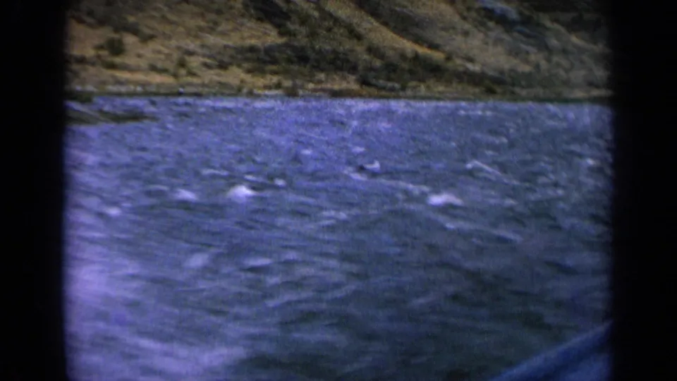 1963 Idaho 8mm frame showing rushing river water with whitecaps and a rugged hillside beyond.