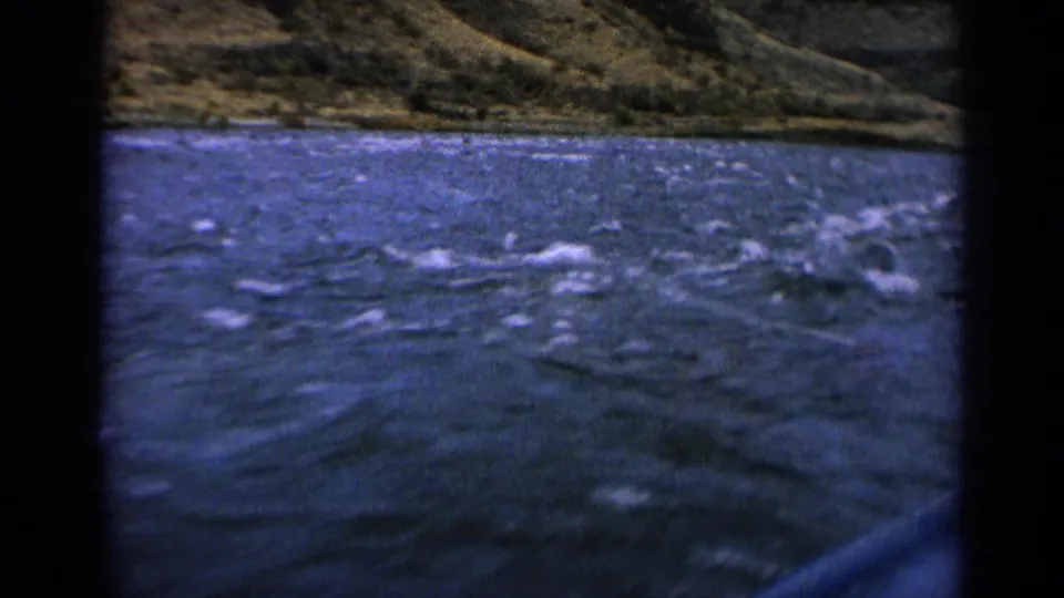 1963 Idaho home-movie frame of turbulent river water and mountain terrain from a boat viewpoint.