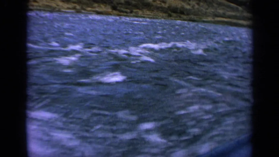 Boat-level 8mm view of rough Idaho river water with a grassy mountain slope beyond.