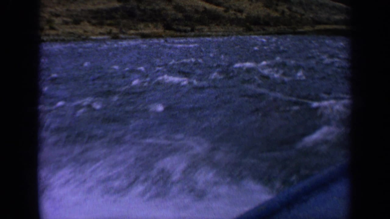 1963 Idaho river boating frame with white spray, choppy blue water, hillside, and a visible boat edge.