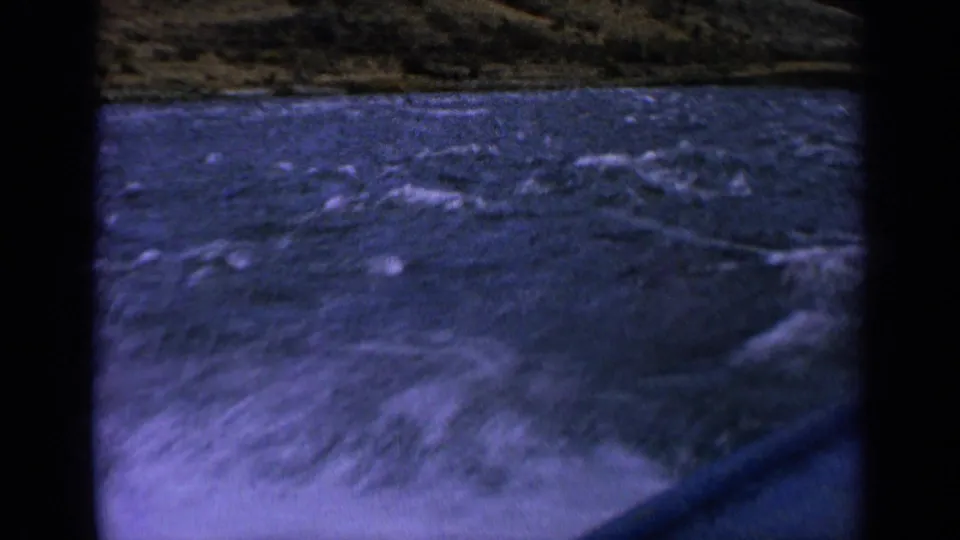 1963 Idaho river boating frame with white spray, choppy blue water, hillside, and a visible boat edge.