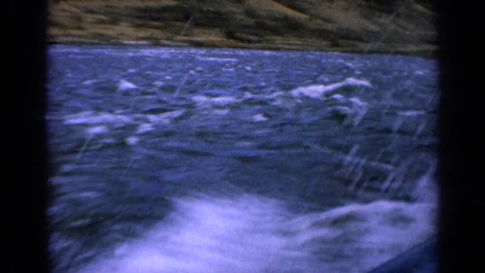 1963 Idaho river footage with white spray and dark blue water rushing past the side of a small moving boat.