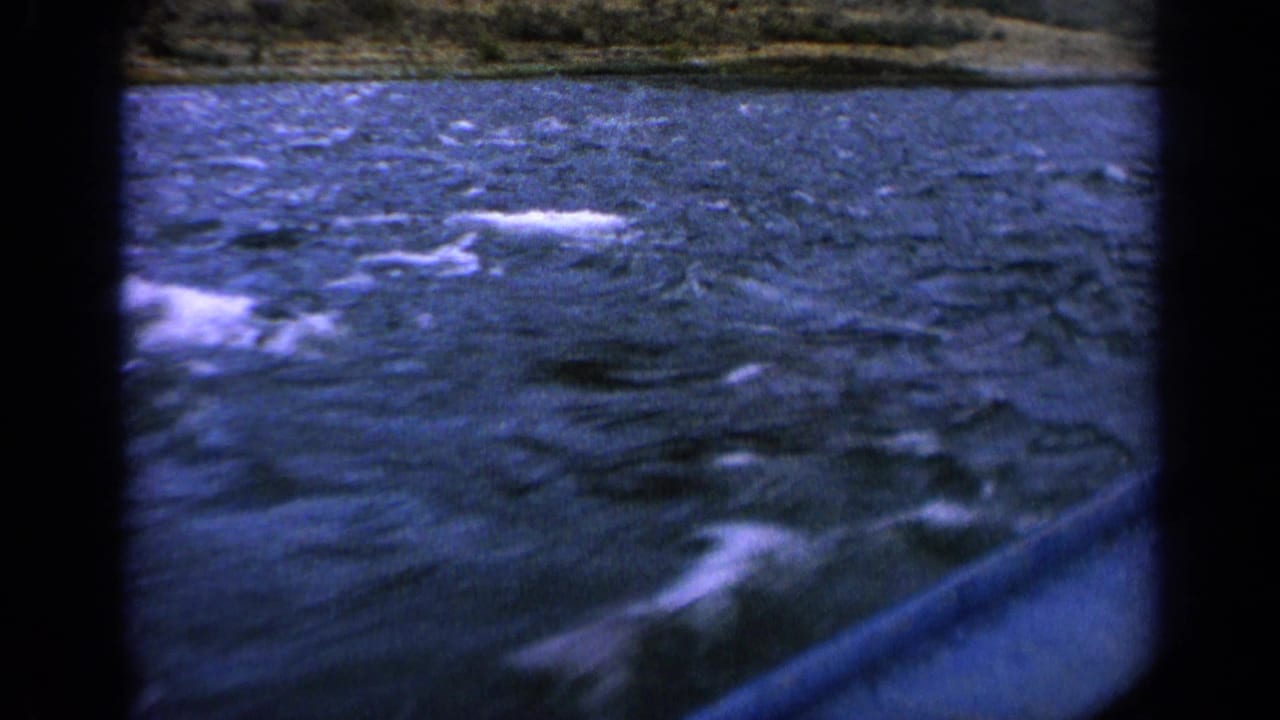 Fast-moving 8mm view of river spray and wake beside a boat, with an indistinct Idaho shoreline in the distance.