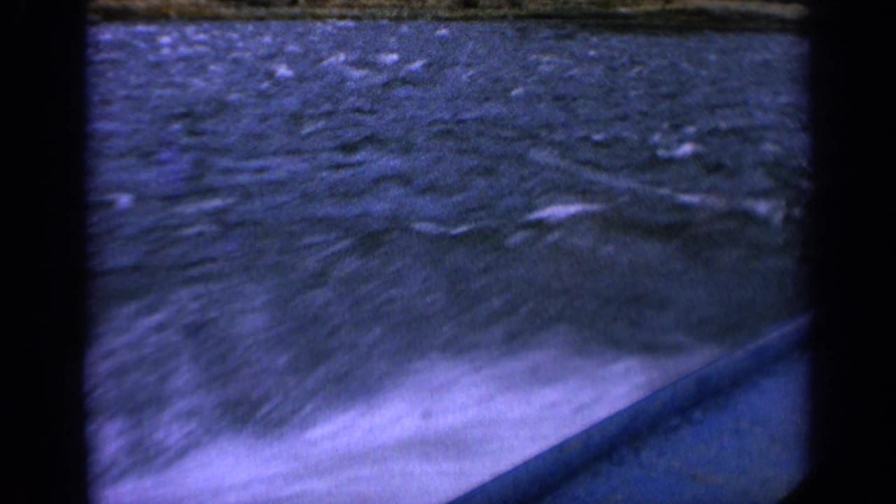 Vintage 8mm boat POV with bright white wake in the foreground and choppy Idaho river water beyond.