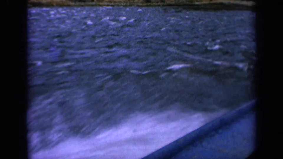 Vintage 8mm boat POV with bright white wake in the foreground and choppy Idaho river water beyond.