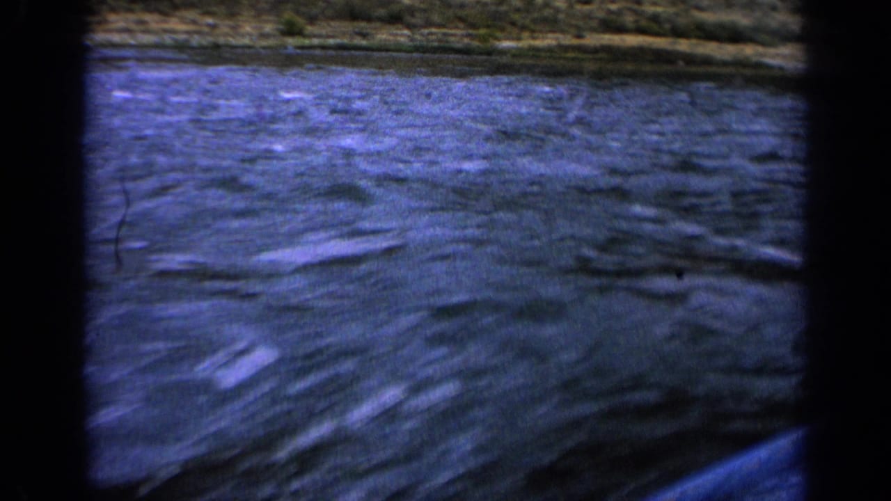 Rippling blue water below a low hillside, with dark vertical film edges.