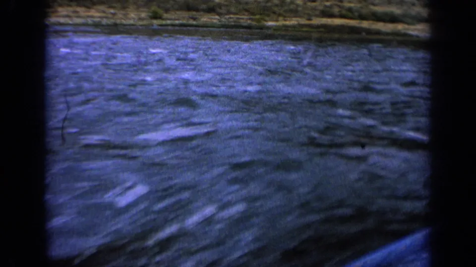 1963 Idaho home-movie frame of blue lake ripples and a distant shore slope, partly bordered by the film gate.