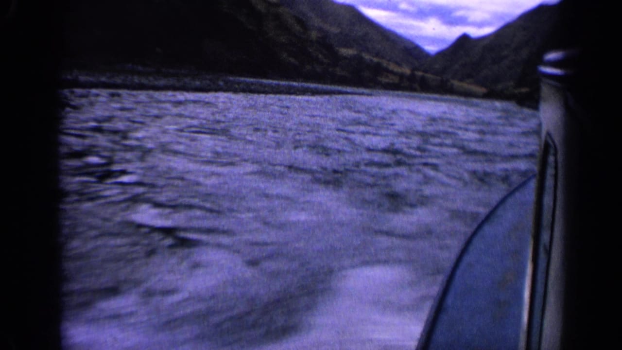 Moving boat view on an Idaho river in 1963, showing water, the boat side, distant mountains, and cloudy sky.