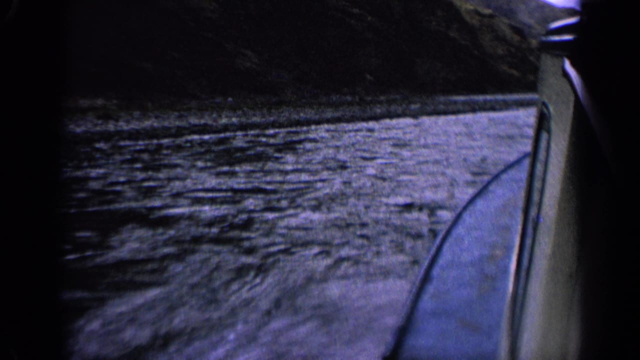 1963 Idaho 8mm view beside a speeding boat, with rippled water, the boat edge, and dark mountain shoreline.