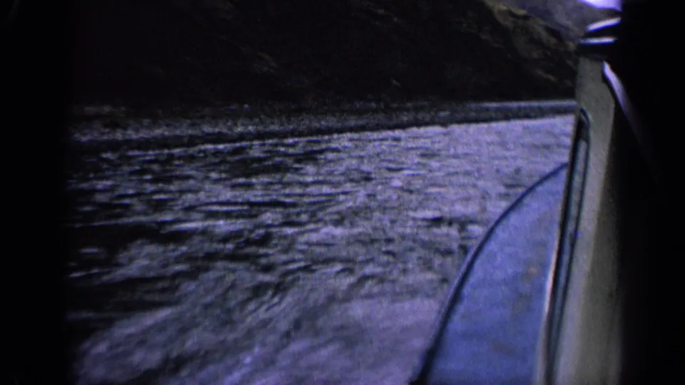 1963 Idaho 8mm view beside a speeding boat, with rippled water, the boat edge, and dark mountain shoreline.