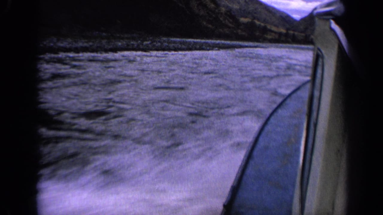 1963 Idaho 8mm frame showing disturbed lake water beside a moving boat, with mountains and cloudy sky beyond.