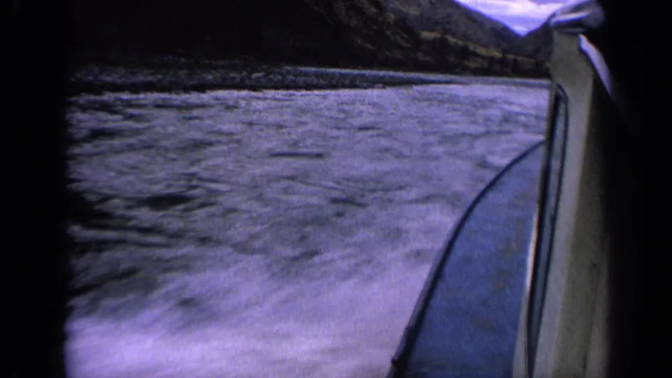 1963 Idaho 8mm frame showing disturbed lake water beside a moving boat, with mountains and cloudy sky beyond.
