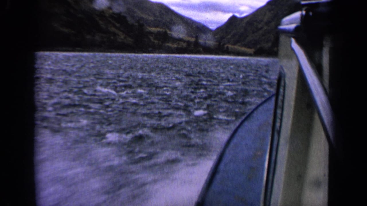1963 Idaho 8mm boat journey view showing choppy lake water, boat side, distant wooded hills, and cloudy sky.