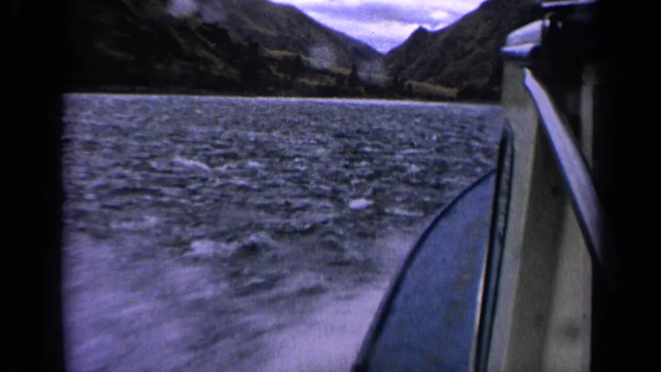 1963 Idaho 8mm boat journey view showing choppy lake water, boat side, distant wooded hills, and cloudy sky.