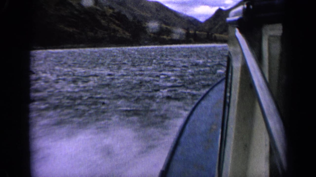 Boat side and wake pass through choppy lake water with mountain slopes in the distance.
