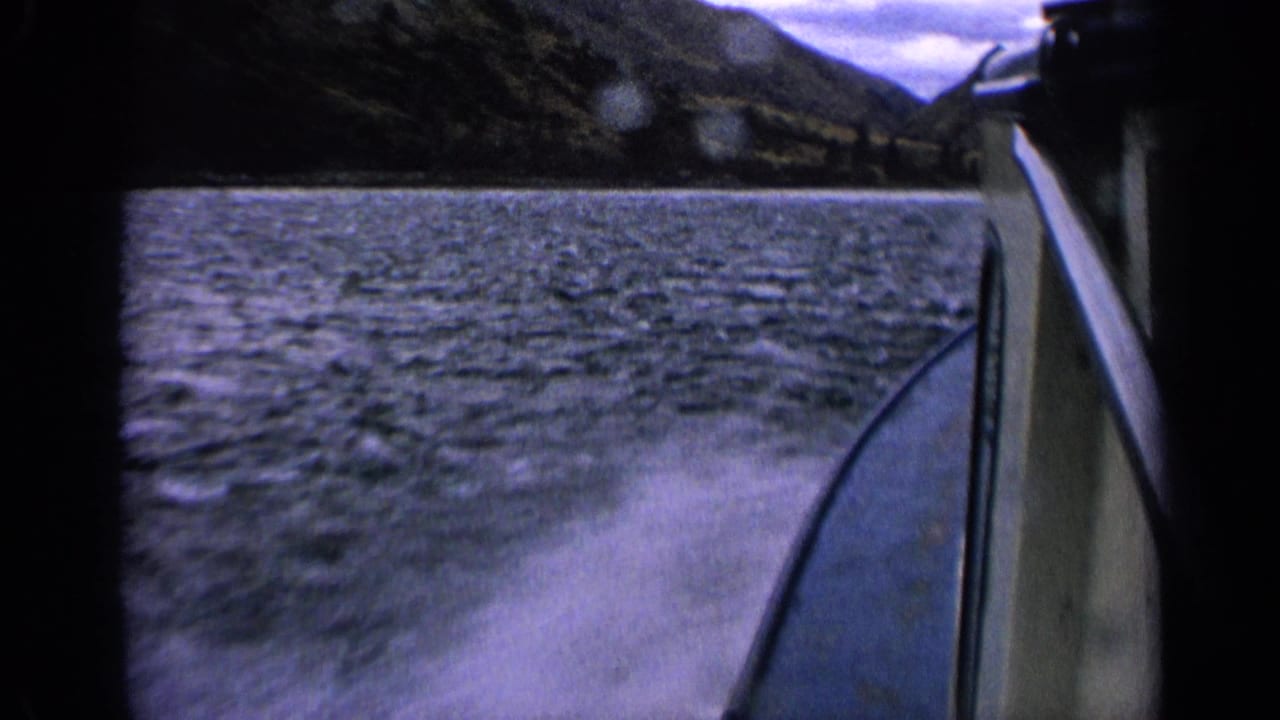 1963 Idaho home-movie frame showing the boat side beside rough lake water and a blurred mountain shoreline.