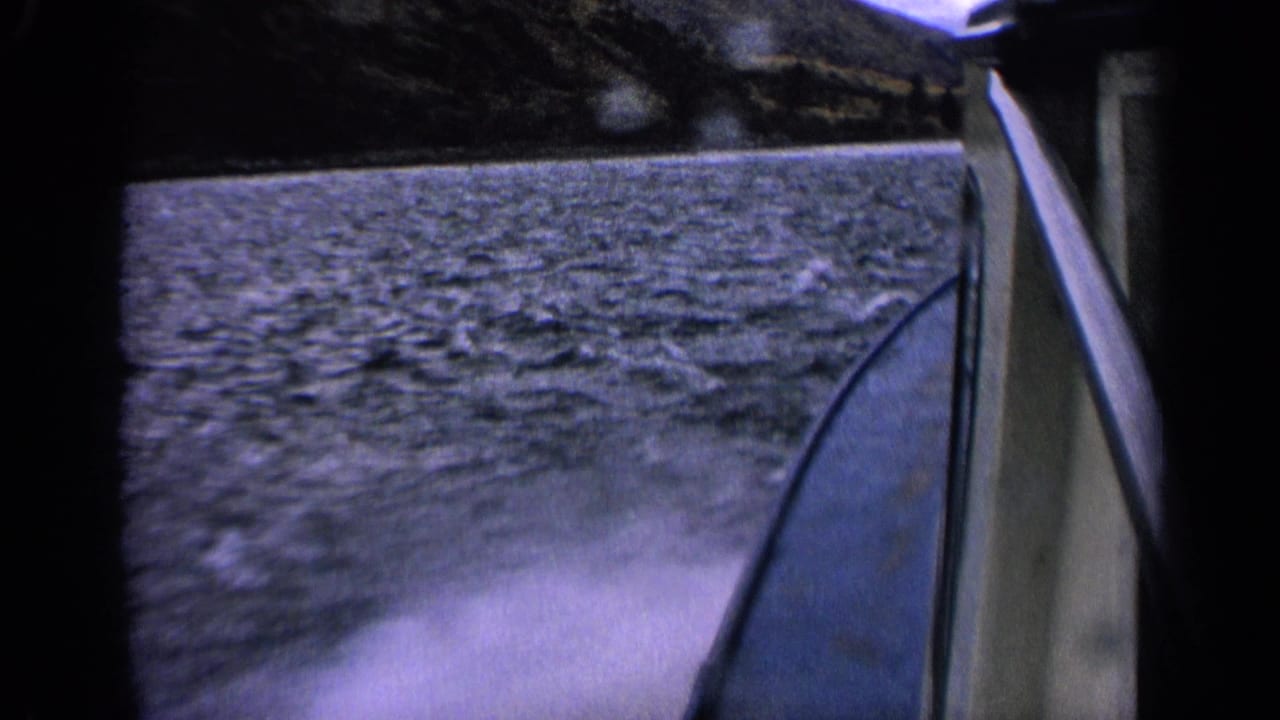 Final 1963 Idaho boat POV frame with rippling lake water, white wake, boat side, and shadowed mountain backdrop.