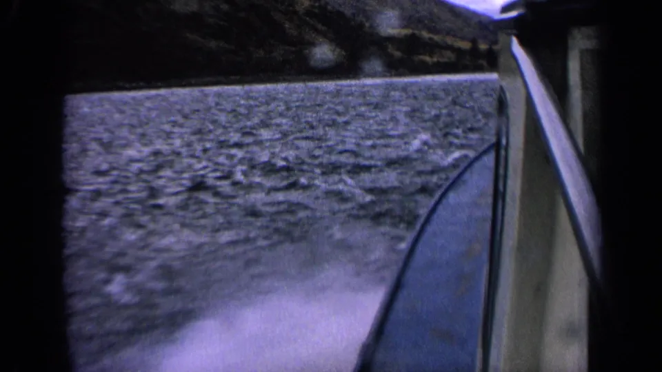 Final 1963 Idaho boat POV frame with rippling lake water, white wake, boat side, and shadowed mountain backdrop.