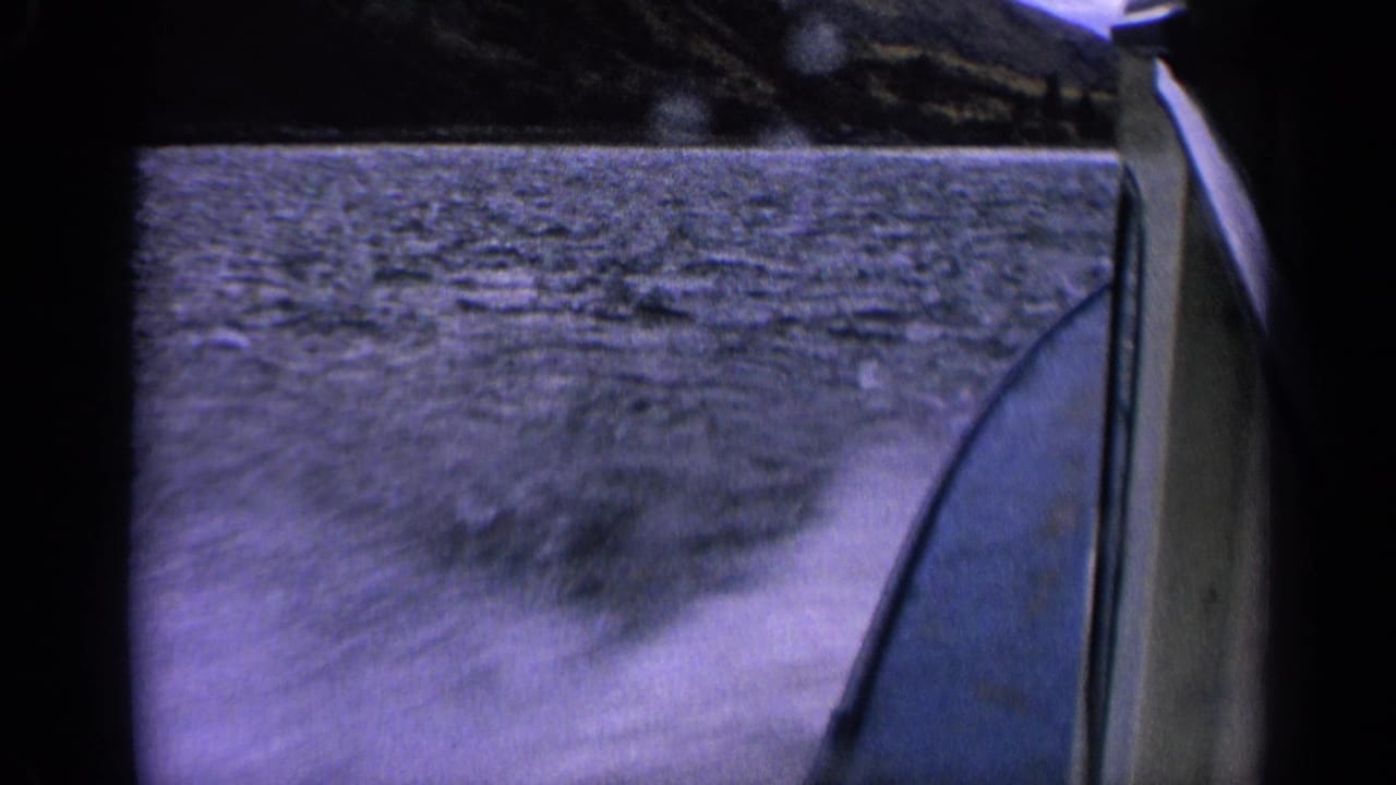 1963 Idaho 8mm boat POV showing the boat edge, lake wake, rippled water, and distant dark shoreline.