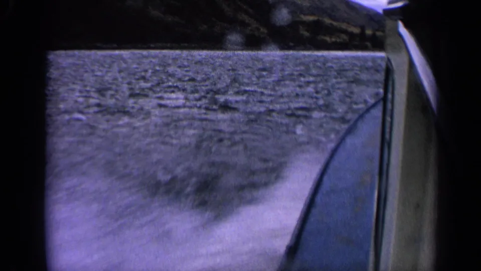 1963 Idaho 8mm boat POV showing the boat edge, lake wake, rippled water, and distant dark shoreline.