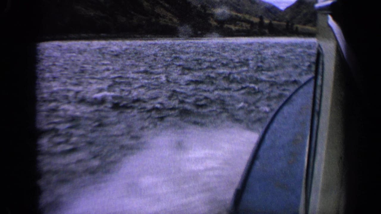 1963 Idaho 8mm frame showing a passenger view of boat wake, lake surface, and dark shoreline beyond.