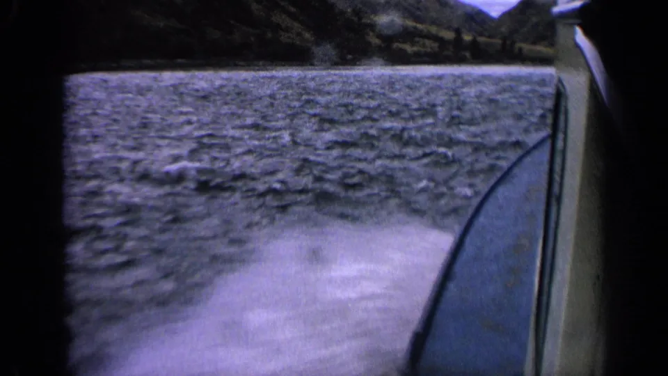 1963 Idaho 8mm frame showing a passenger view of boat wake, lake surface, and dark shoreline beyond.