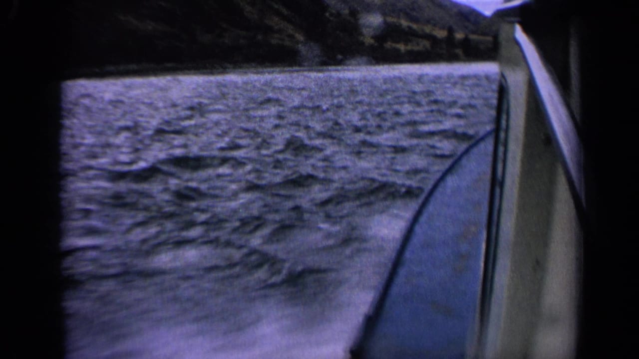 Rippling lake or river water seen beside a moving boat, with shoreline hills beyond.