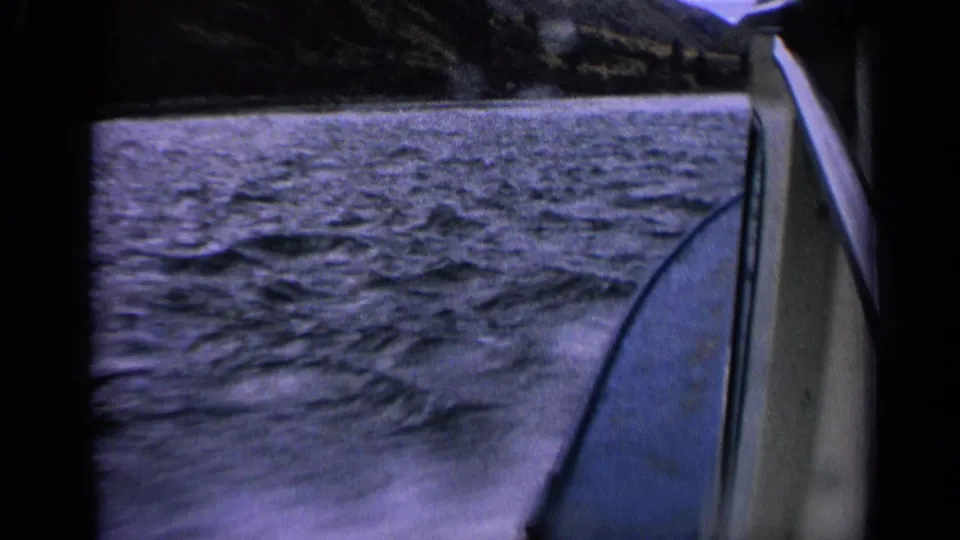Passenger view from a moving boat in Idaho, 1963, with textured water, a narrow wake, the boat side, and distant sloped shoreline.