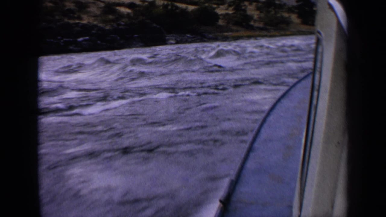 Moving-boat view on an Idaho river in 1963, with rough blue-gray water, whitecaps, boat trim, and a dark wooded bank.