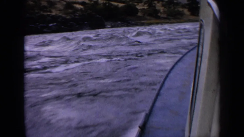 Moving-boat view on an Idaho river in 1963, with rough blue-gray water, whitecaps, boat trim, and a dark wooded bank.